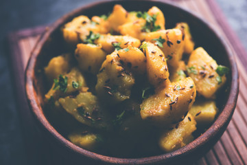 Jeera Aloo is a Indian main course dish which goes well with hot puris, chapatti, roti or dal. served in a bowl over moody background. selective focus