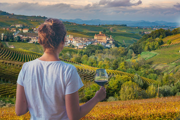 girl holding a glass of red wine looking amazing green vineyards in the italian region of Piedmont, Alba, Barolo town, langhe Monferrato region, Italy - obrazy, fototapety, plakaty