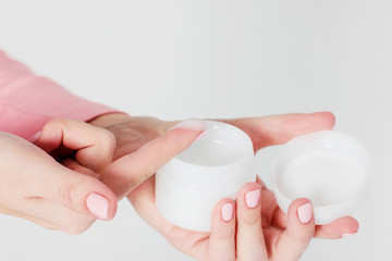 Beautiful delicate women's hands with pink manicure holding jar with caring cream isolated on gray background close up