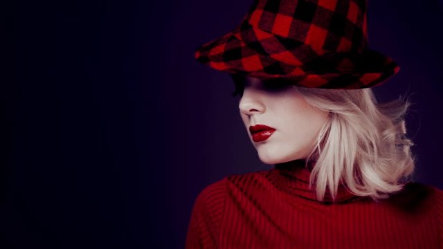 Woman in red hat with red lips posing before camera. Girl in retro fashion on dark background. Cosmetic heart-shaped beauty spot on the girl's cheek. Beautiful bright makeup, red lipstick. Incognita.