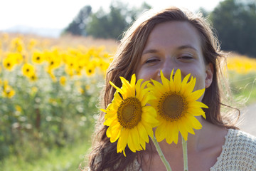 handsome teenage girl brunette with sunflower enjoying nature and laughing on summer sunflower field