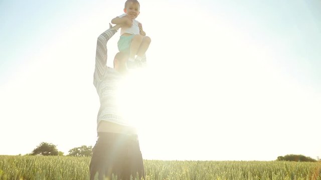 Strong father lobbed son in the sky. Playing with him at sunset in the wheat field