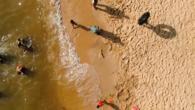 Aerial view move along small tropical, beach with indistinct Asian families and kids visible along the gulf of Thailand in Cambdodia, Southeast Asia. Camera lifts to reveal wider view.