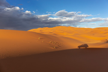 View of a very wide desert sand dunes with visible foot marks from some visitors and shadow of a car