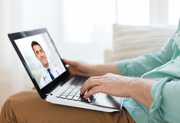 medicine, technology and healthcare concept - close up of man or patient having video call with male doctor on laptop computer at home