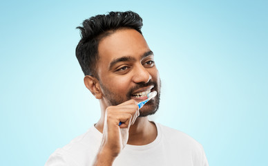 oral care, dental hygiene and people concept - smiling young indian man with toothbrush cleaning...