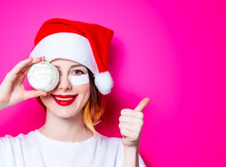 Woman using eye patch for her eyes in Santa Claus hat with cream on pink background isolated. Portrait of natural  and true female as usually they are looks like