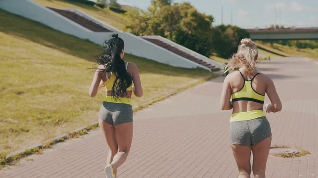 Two running fitness women joggin in urban city at morning. Athletic friends running in green sport wear in slow motion. Healthy lifestyle concept