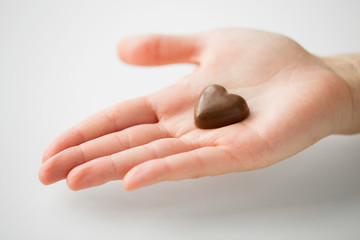 valentines day, sweets and confectionery concept - close up of hand holding heart shaped chocolate candy