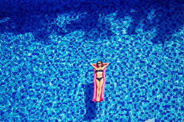 copy space spf and sunscreen beautiful brunette girl floating in the pool water.woman swimming and relaxing on pink inflatable mattress in blue swimmingpool remote work and freelance