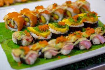 The row of rolled sushi with shrimp orange eggs and sea weed on the white ceramic tray in the incandescent light of restaurant.