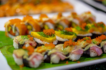 The row of rolled sushi with shrimp orange eggs and sea weed on the white ceramic tray in the incandescent light of restaurant.