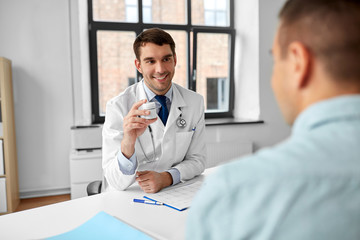 medicine, healthcare and people concept - smiling doctor showing jar with drug to male patient at...