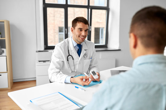 Medicine, Healthcare And Diabetes Concept - Smiling Doctor With Glucometer And Insulin Pen Device Talking To Male Patient At Medical Office In Hospital
