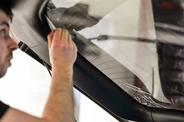 Man squeegeeing water from the window and window tinting film. Professional car window tinting services