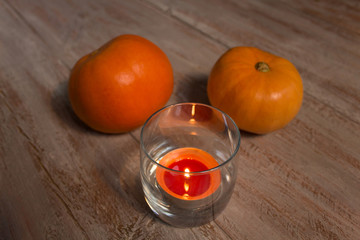 Orange pumkins with colorful candle in the glass on the wooden boards.