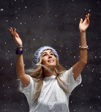Blonde woman in light blue knitted hat happy smiling sitting under snowflakes winter time 
