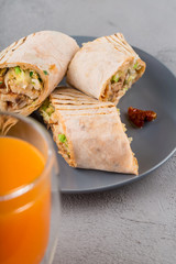 Close-up of Doner kebab rolls on a plate with dried tomatoes and orange juice.