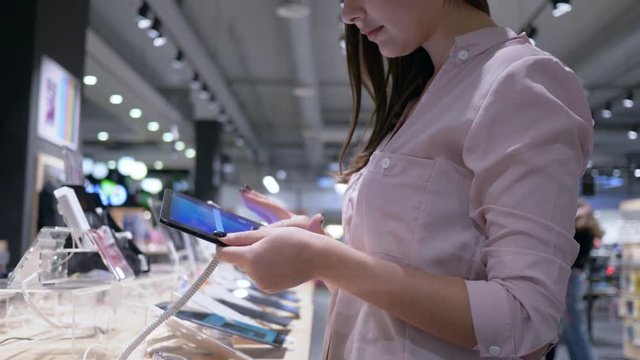 electronics store, beautiful young girl uses latest modern tablet computer and think about buying