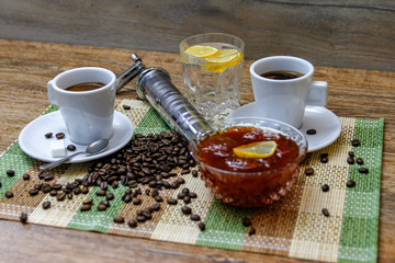 Coffee on wooden table and old manual coffee grinder. Mineral water and traditional plum jam with lemon. coffee beans spilled on the table.