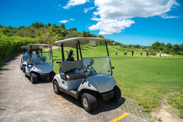 Golf carts parking near golf course with golfers and caddie are in competition,blue cloud sky background.