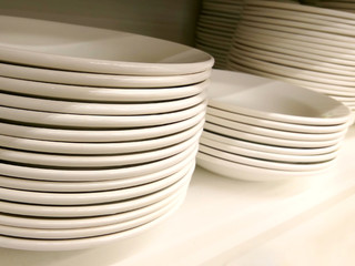 Obraz premium Stack of new clean white plain plates and bowls on the shelf