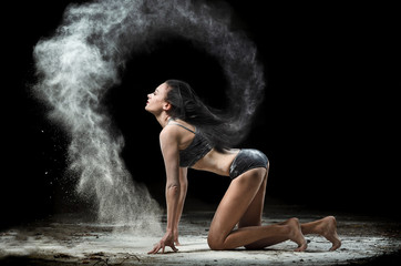 Graceful woman posing in a cloud of dust on a black background