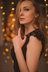 Portrait of Beautiful Woman in Lights. Fashion Dress and MakeUp. Christmas Santa. Elegant Lady in Red Dress over Christmas Tree Lights Background. Happy New Year.