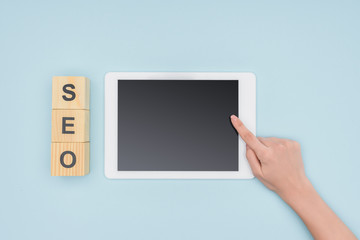 Top view of female seo manager pointing at digital tablet near wooden cubes  on light blue background