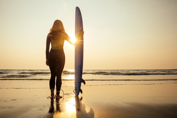 Beautiful woman in a diving suit for swimming surfing in the Indian Ocean on the background sunset sky and waves.professional surfer girl in a wetsuit doing sports at sea.extreme, adrenaline and youth