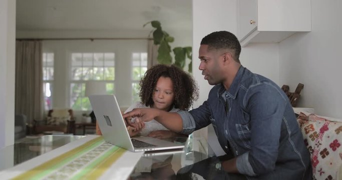 African American father helping daughter with homework using laptop