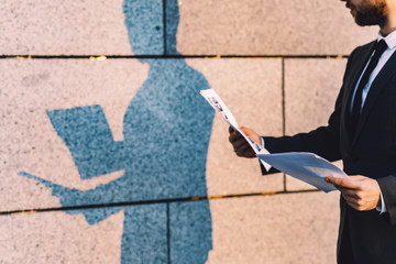 Close-up businessman  in a classic suit holds and reads a business document in paper form. Outdoors a man and his shadow on the wall.