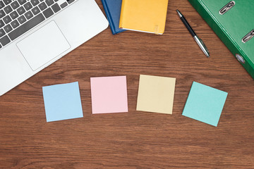 top view of four sticky notes, laptop and office supplies on wooden desk