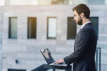 Businessman outdoors on the background of a business building working on a laptop