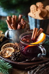 Mulled wine or vin brule in a glass mug with star anise, cinnamon sticks and a slice of orange with traditional festive Christmas decorations at the mackground