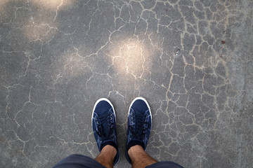 Point of view of a man with blue shoes standing on asphalt floor.