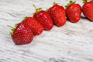 An arc of fresh ripe red strawberries lies on a light textured wooden table. Close-up. Copyspace
