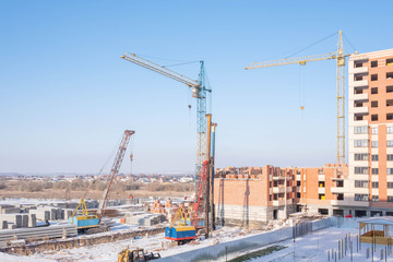 Fototapeta na wymiar Crawler cranes, piles, concrete slabs and cranes on the construction site near the multi-storey building. The process of driving piles. Translation: 