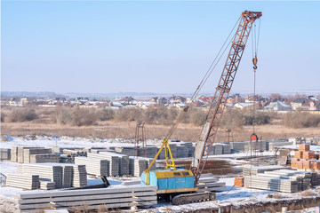 Fototapeta na wymiar Lifting equipment. Crawler crane, piles and concrete slabs at a construction site near a multi-storey building. Translation: 