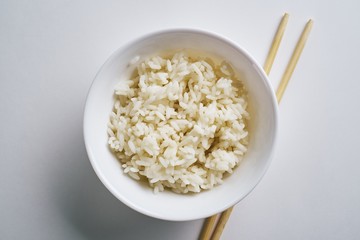 Top view of boiled rice with chopsticks on a white plate isolated on white background