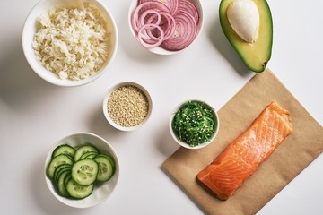 Fresh seafood recipe. Shrimp salmon poke bowl on craft paper, sweet onions, avocado ,Chuka Salad, white rice, cucumber, portioned with white sesame. poke bowl, top view, White background