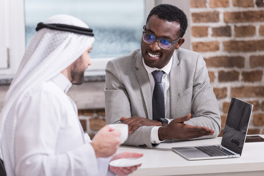 African american businessman showing laptop to arabian partner in office