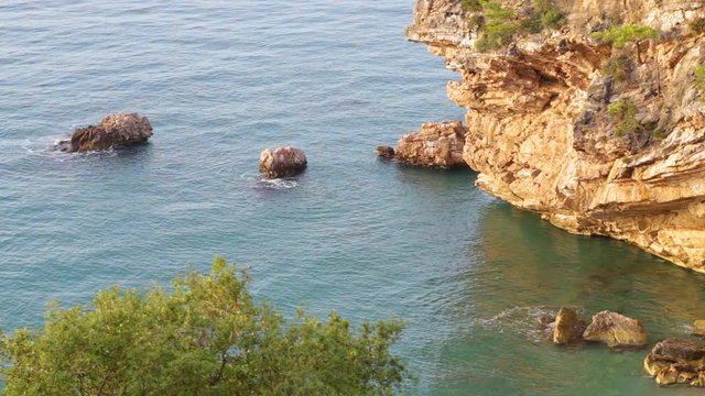 Beautiful morning seascape. Aerial top view of charming calm blue sea water, huge rocks and stones, green trees. Scenic summer marine background. Real time full hd video footage.