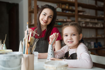 Child girl with mother at pottery workshop painting pottery
