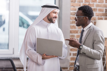 African american businessman pointing at laptop and looking on arabian partner