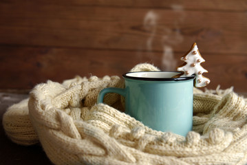 A blue cup with hot tea and a white knitted scarf on a dark wooden background.