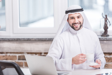 Arabian businessman drinking coffee near laptop in office