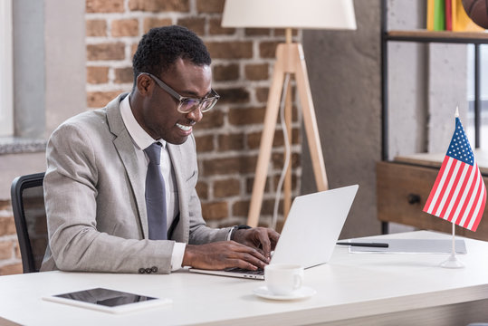 African american businessman sitting at office desk and using laptop - Powered by Adobe