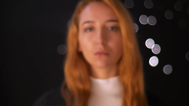 Gorgeous caucasian redhead woman is walking from blurred dark background and focused looking at camera with relaxed pretty face indoors, motion illustration