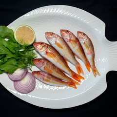 Red mullet fish with rocket leaves on plate with black background